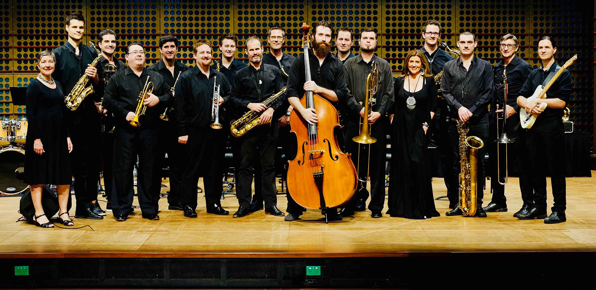 An image of the Brisbane Jazz Orchestra members standing on a stage with their instruments.